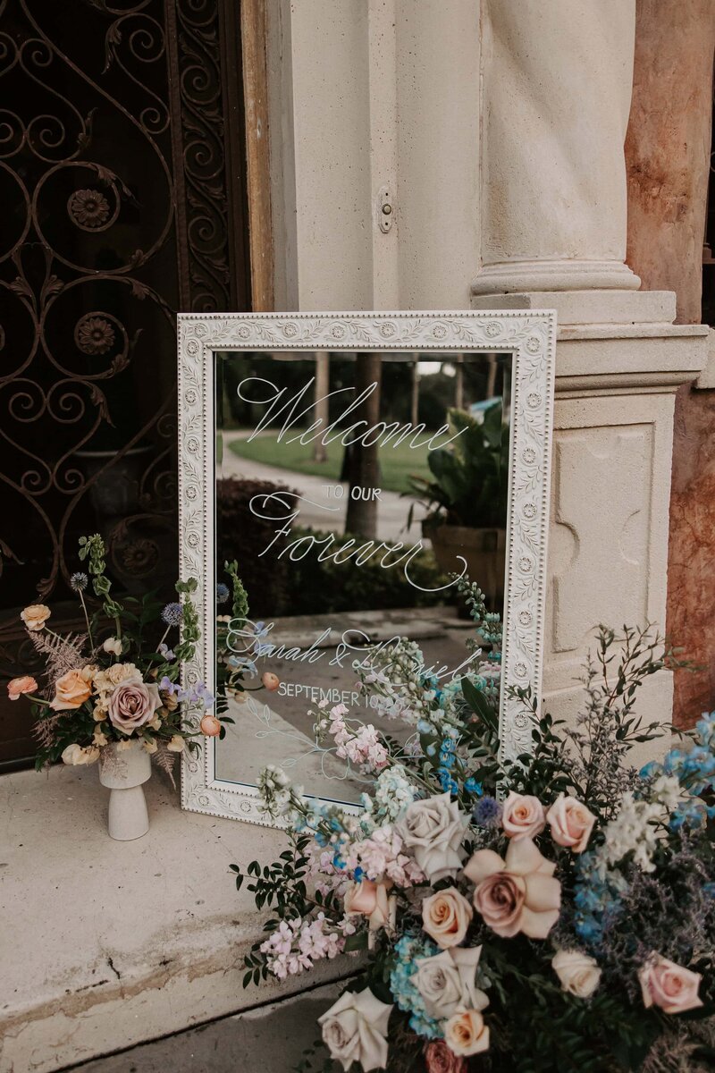 Ornate white-framed mirror with calligraphy writing, surrounded by pastel floral arrangements