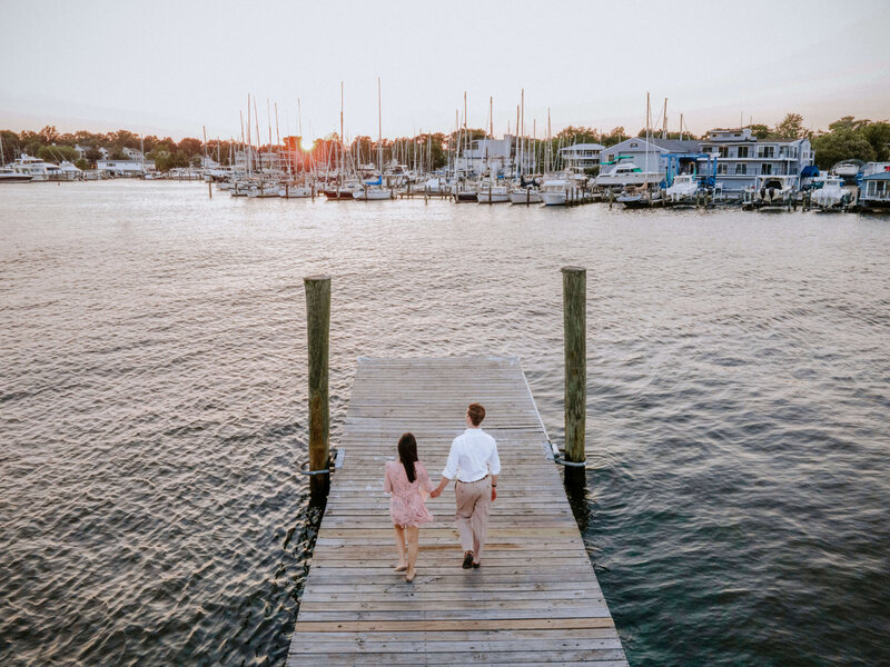 engaged-couple-walking-on-dock-during-sunset