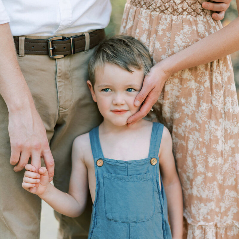 Little boy holding the hands of his parents and wearing blue overalls