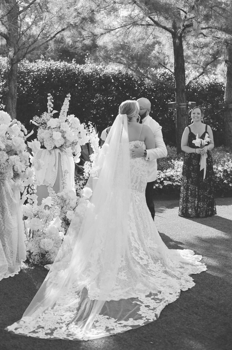A black and white image of a couples first kiss at wedding