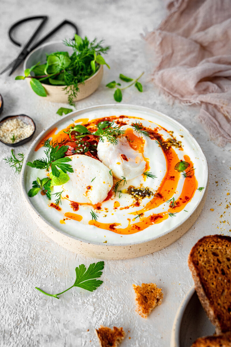 A mouth-watering plate full of yoghurt, poached eggs and garnished with greens on top