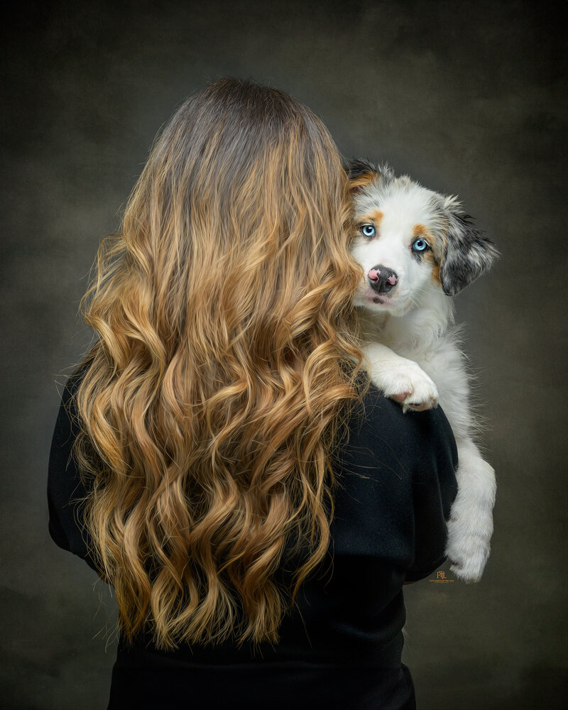 Immerse yourself in the elegance of fine art photography with our captivating portraits of people and their pets in Vancouver. This unique image showcases a woman with flowing hair holding her blue-eyed puppy, beautifully highlighting the intimate connection and serene moment they share. At Pets Through the Lens, we create timeless, artistic portraits celebrating the deep bond between humans and their beloved pets.