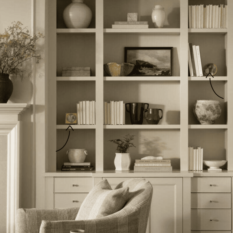 A chair positioned before a bookcase, with a vase atop a table and picture frames adorning the wall.