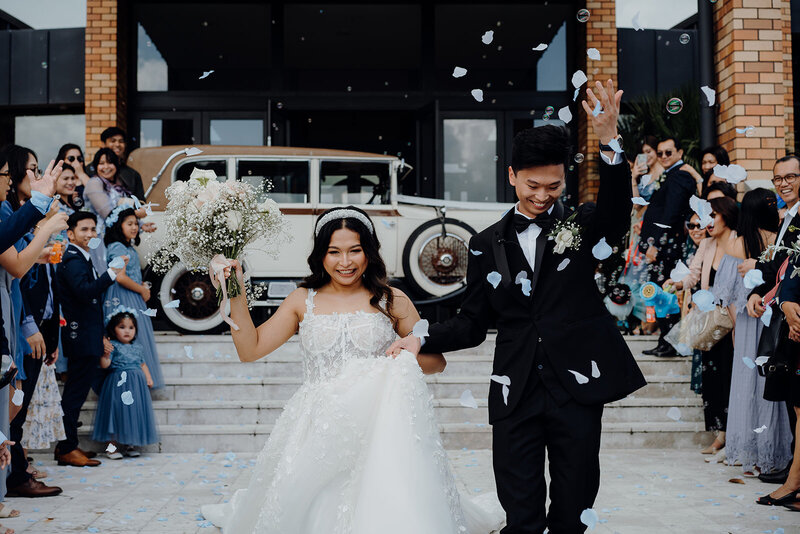 A newly married couple walking down the stairs of the church while their guests throw blue and white confetti on them and they're photographed by Waikato Wedding Photographer Haley Adele Photography