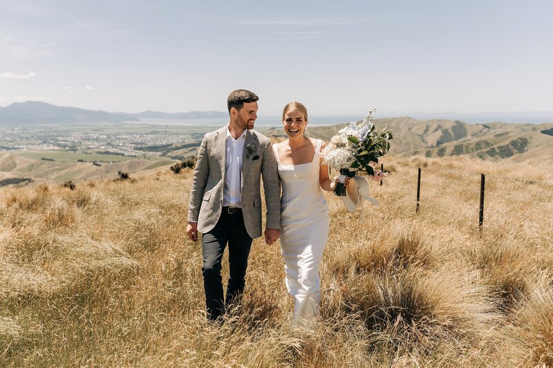 a bride and groom walk through gold grass on mountaintop in blenheim on their wedding day