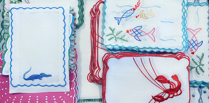 Flatlay of whimsical table linens featuring embroidered lobster, fish and alligator withh scallopped edges