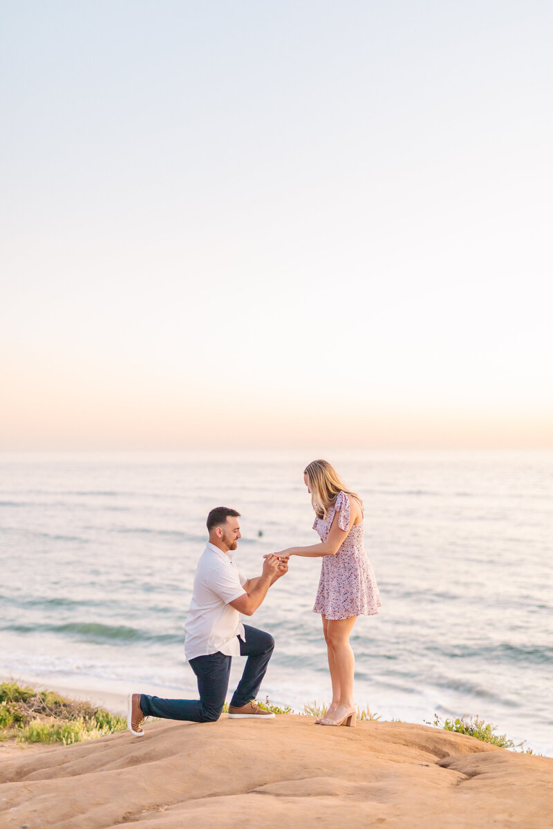 The ocean behind them, Mike proposes to Anna down on one knee at Carlsbad Cliffs.