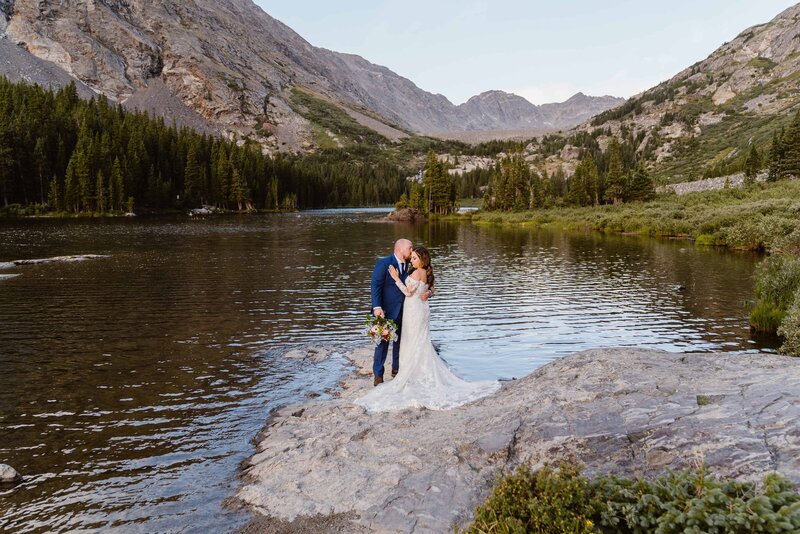 couple stands on a rock at the edge of an alpine lake in Breckenridge, Colorado during their elopement with Alpine Vows