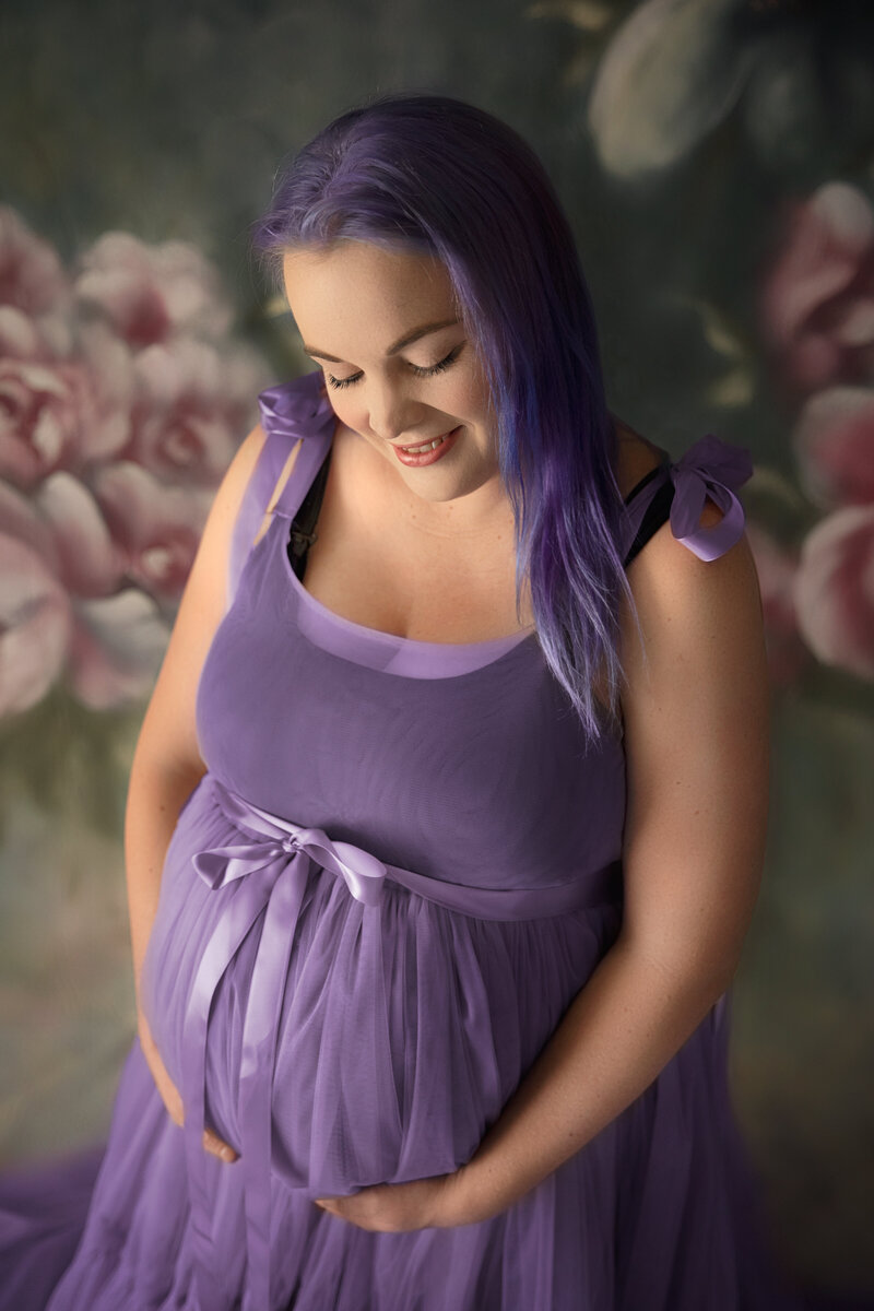 expecting mother in studio shoot, stunning purple dress and hair, with pink flower backdrop