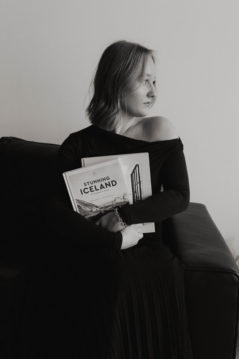 A woman looking over her shoulder holding travel books as she poses for a photo