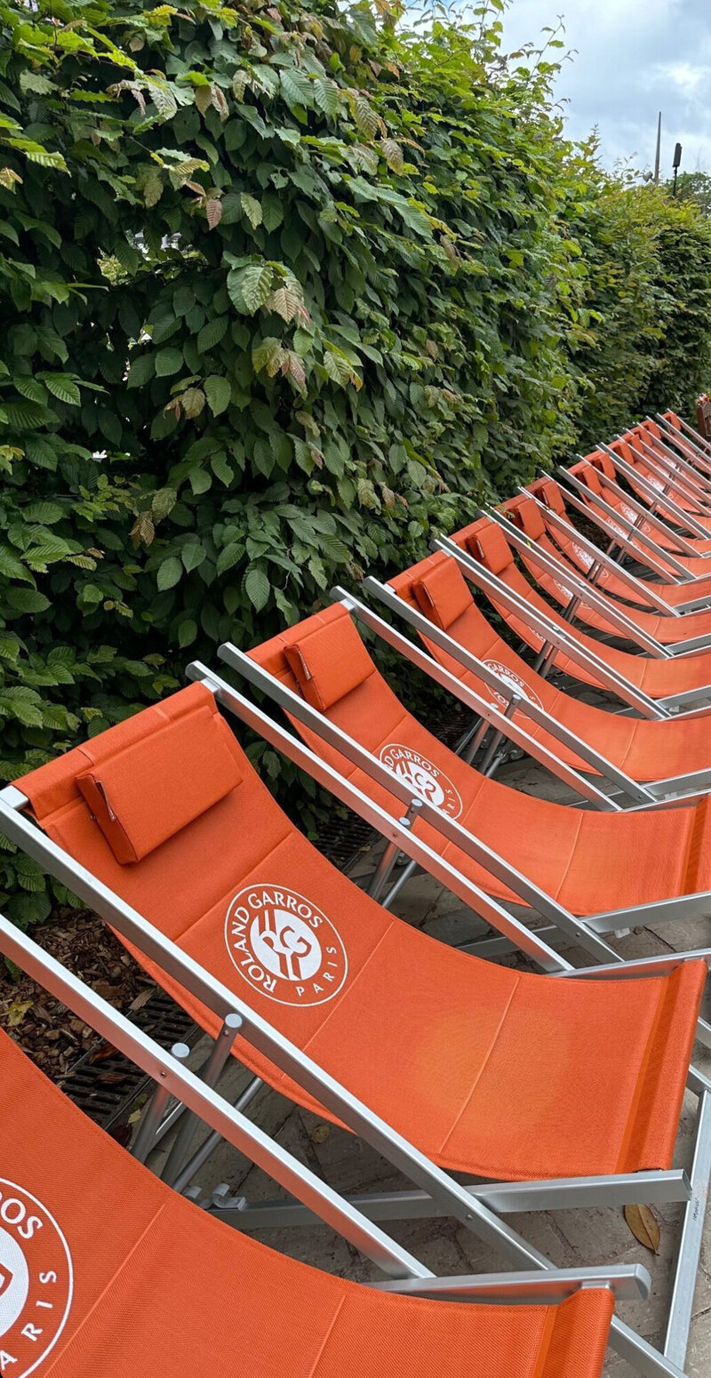 Row of orange Roland Garros lounge chairs by a leafy hedge