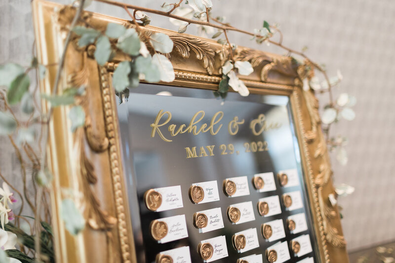 vintage gold escort mirror with greenery on top with wedding guest white place cards with gold wax seals adhered to the mirror