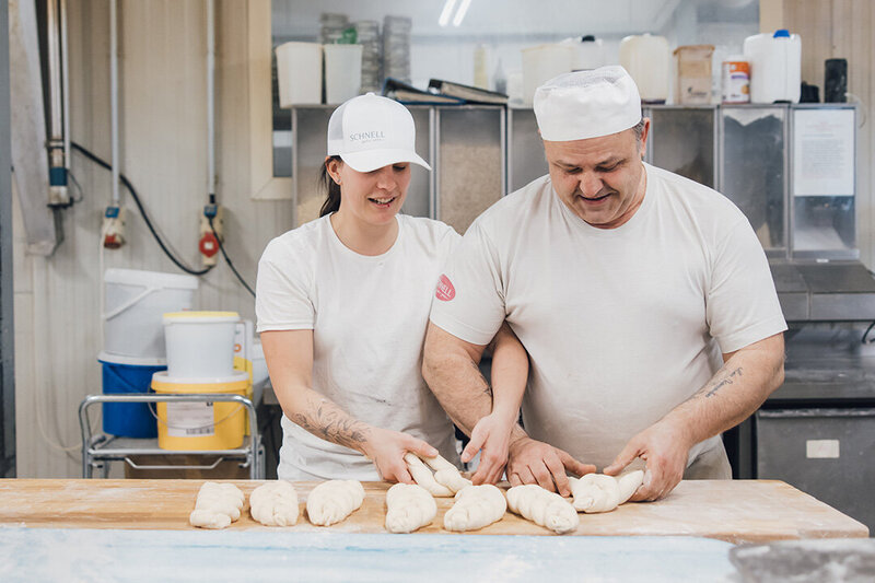 Bäckerin und Bäcker formen zusammen einen Hefezopf und lachen - Bäckerei Schnell in Feldkirch