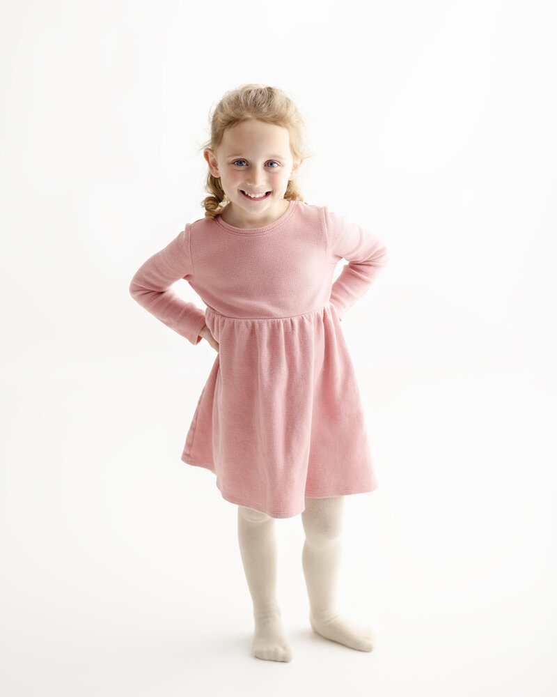 This milestone portrait of a girl in a soft pink dress exudes confidence and joy, all captured in a clean and bright studio setting.