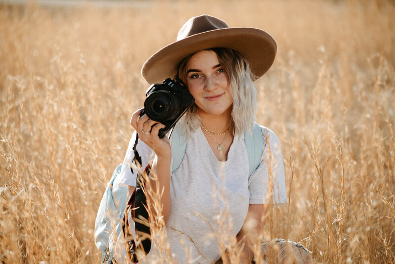 Blonde female with a brown hat sitting with camera in a field