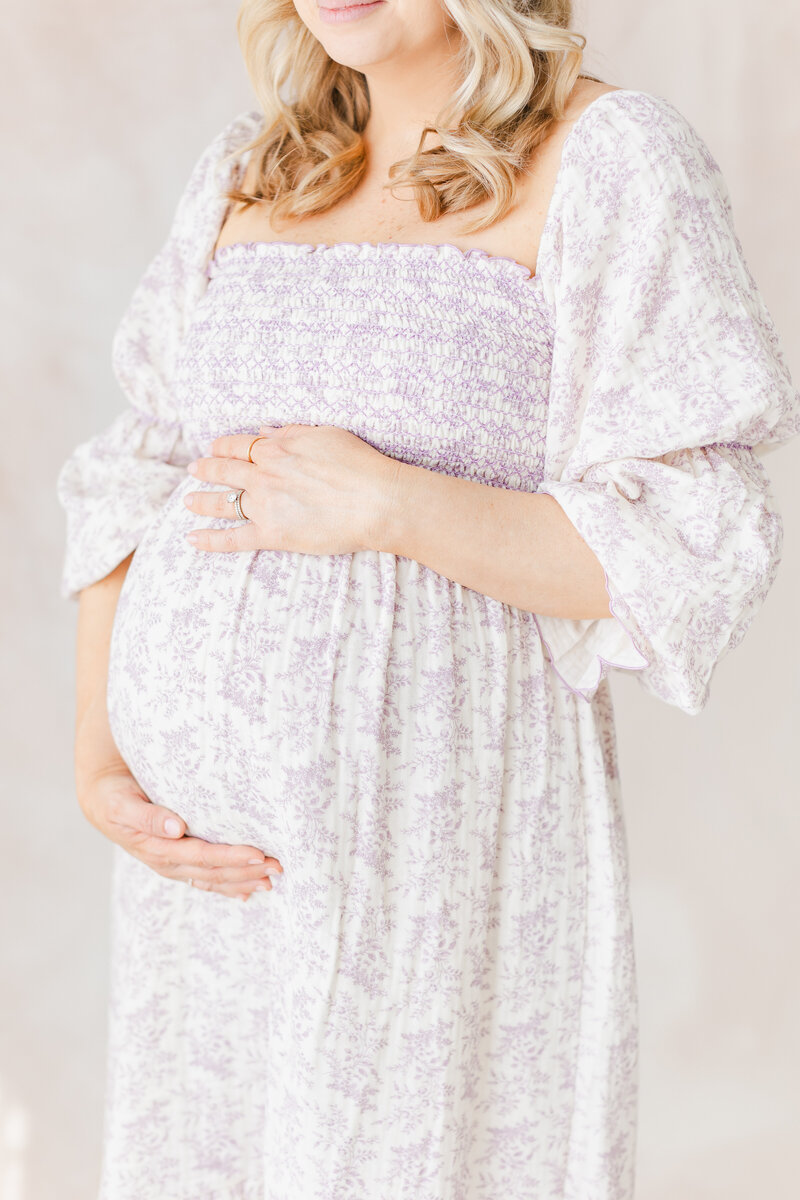 Pregnant mama holding her belly wearing a maxi purple and white flower long sleeve dress for her Northern Virginia Newborn Photography session