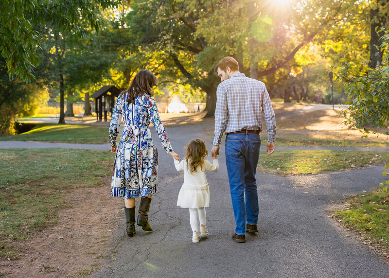 Family holding hands and walking a in NJ park in front of fall leaves with a sun flare.