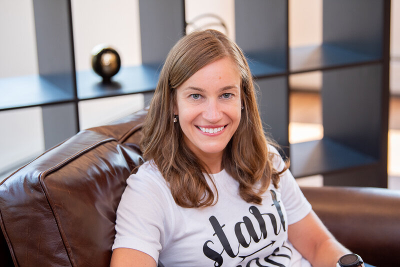 A female coach is smiling for her headshot and sitting on a brown couch in Fairfield, New Jersey.