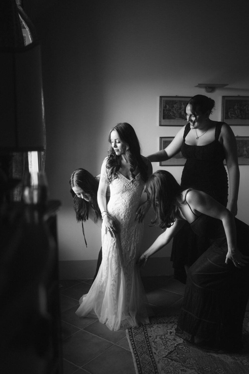 Elopement Ideas with Family | Three bridesmaids help an eloping bride tidy up her dress in Tuscany with dramatic cinema style lighting