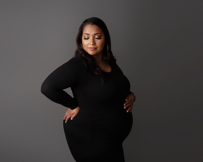 Studio maternity portrait of Latin expectant mom in black dress with gray backdrop in Jacksonville, FL.