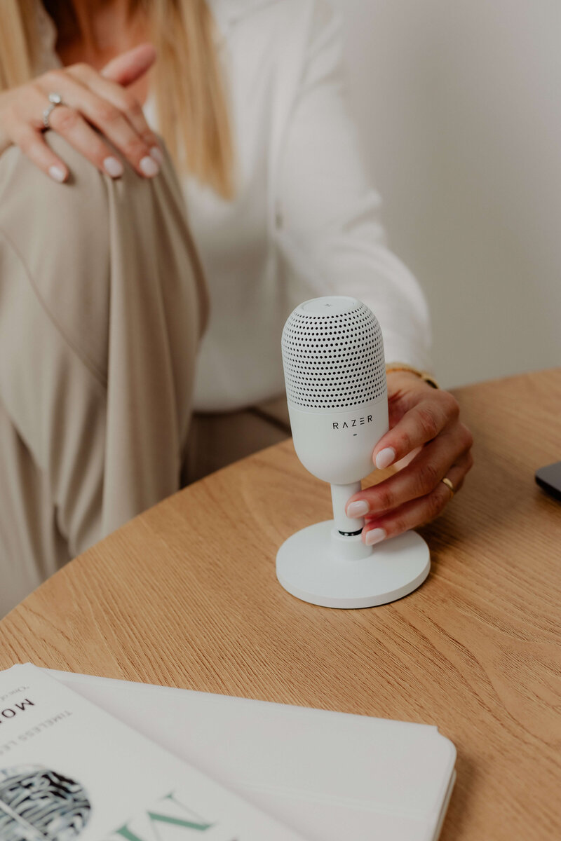 A women sitting at a table with her hands on a microphone. 