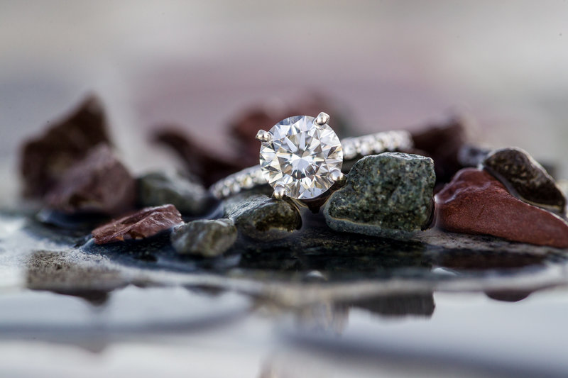 Close-up of an engagement ring glistening on water-washed stones during a romantic and adventurous destination engagement session.