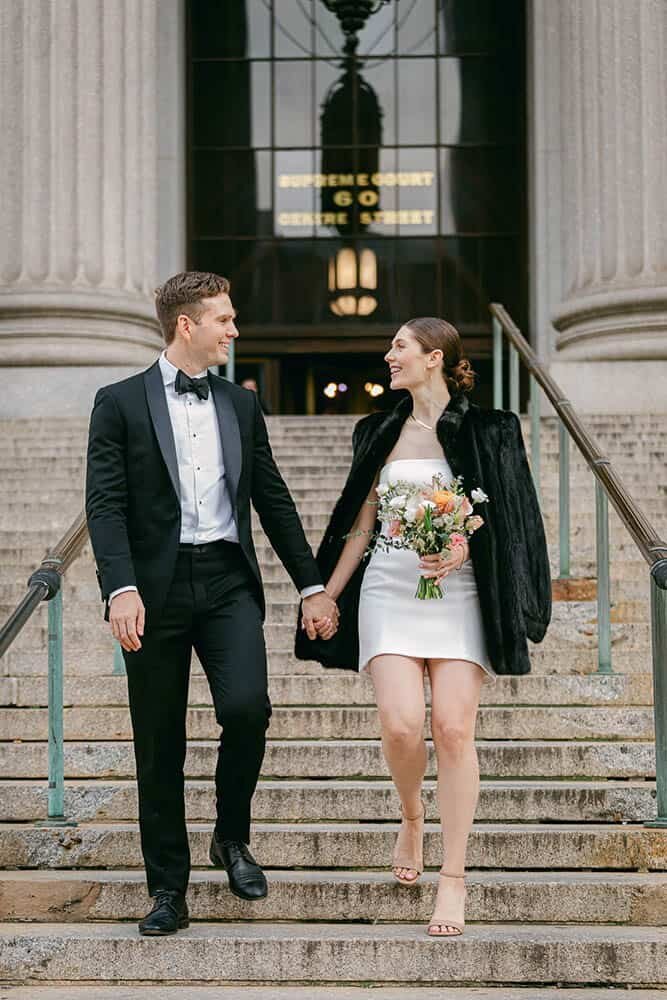 A bride and groom walk down the steps of the Supreme Courthouse in Manhattan after a civil wedding ceremony.