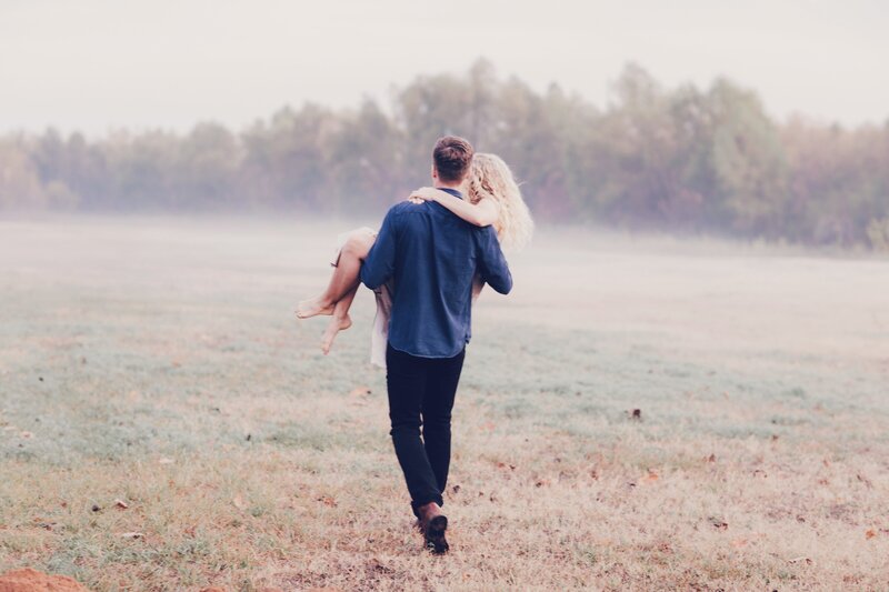 A engagement photographer captures a man carrying a woman in a field during their engagement photo session Britt Elizabeth