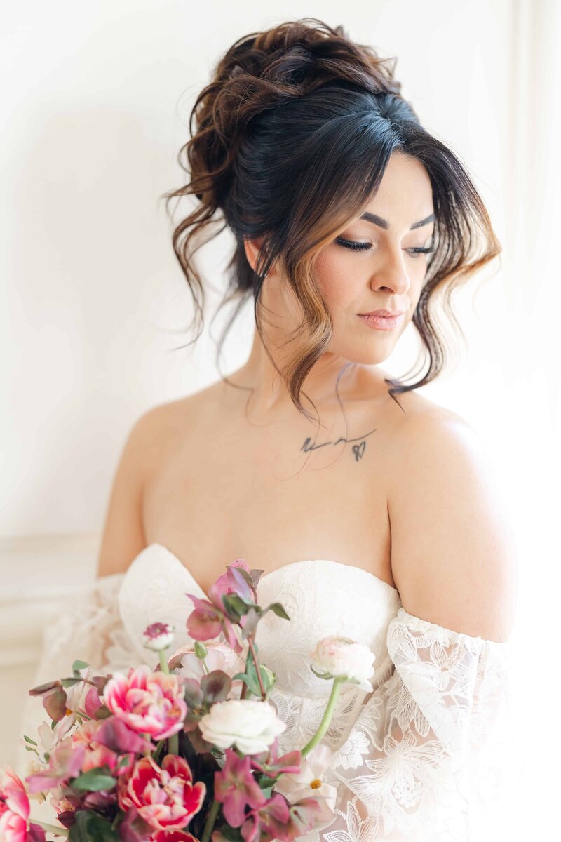 Bride with tattoo on her collarbone holding a bouquet of pink flowers