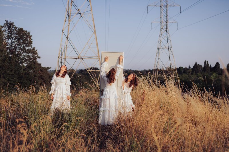 3 images photoshopped into one of young, red-headed woman in multiple poses wearing a flowy white dress in a field with a white door and powerlines.