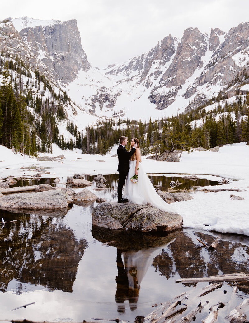 Couple stands on a rock at Dream Lake in Rocky Mountain National Park after their elopement at Sprague Lake, Colorado