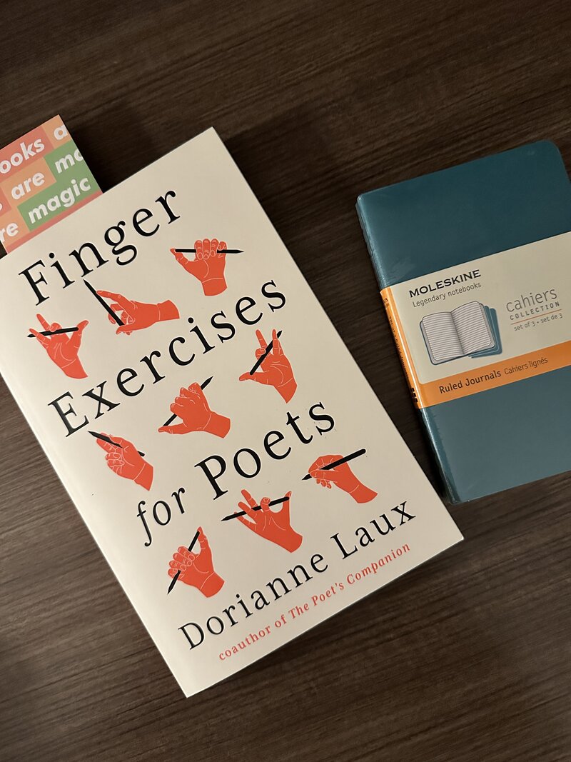A photo of a book called "Finger Exercises for Poets" by Dorianne Laux on the left, with a Moleskine notebook for writing on the right.