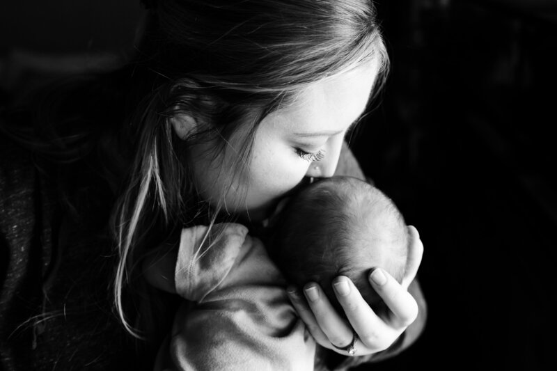 up close black and white image of mom kissing newborn daughter's cheek