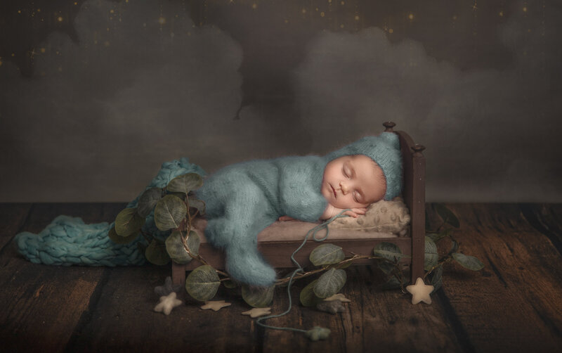 "Sleeping newborn peacefully curled up in a cozy bed, surrounded by soft blankets and pillows, captured in a serene fine art photography session in Ottawa."