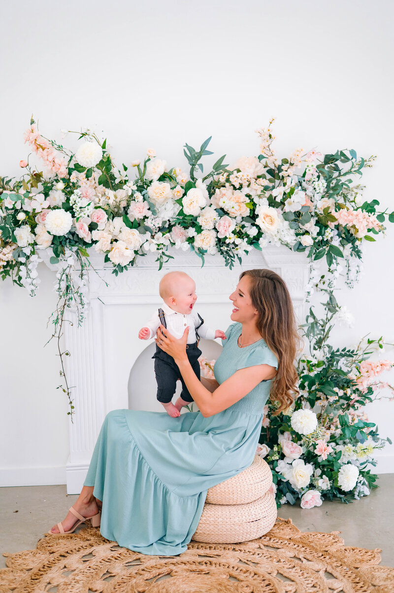Mother lifting baby during a floral motherhood studio session
