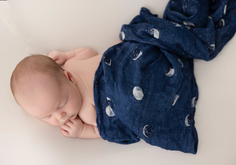 two-week old newborn boy lying on posing table covered in a wrap with small moons on it. 