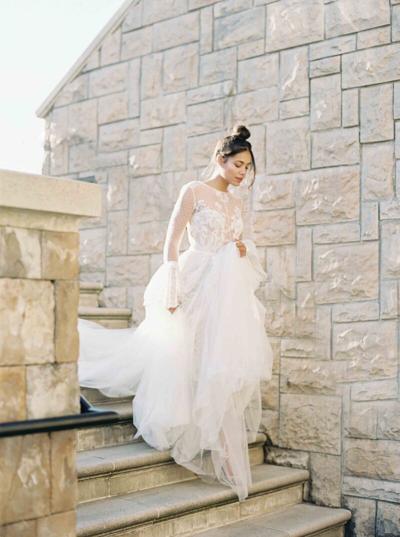 Seattle Film Wedding Photographer - ethereal bride walking down stairs with a top knot bun holding her tulle gown with lace top and long sleeves