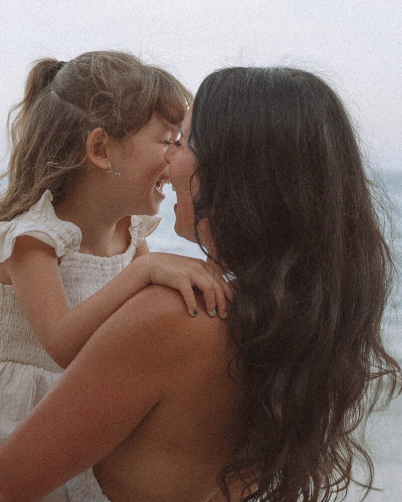 Mother and daughter sharing a joyful nose-to-nose laugh by the ocean in Laguna Beach.