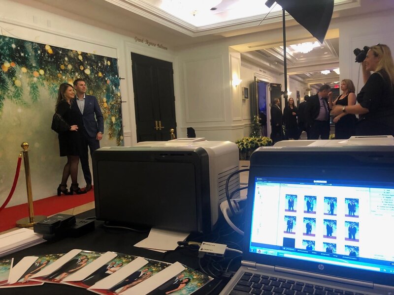 Beautifully decorated holiday event venue featuring Christmas trees, lighting, and an onsite printing station setup with professional studio lights for event photography