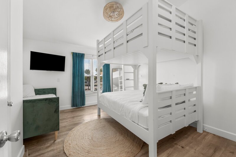 Upstairs queen bunk bed setup with rollaway and teal curtains in a stylish bedroom, perfect for groups visiting Panama City Beach.