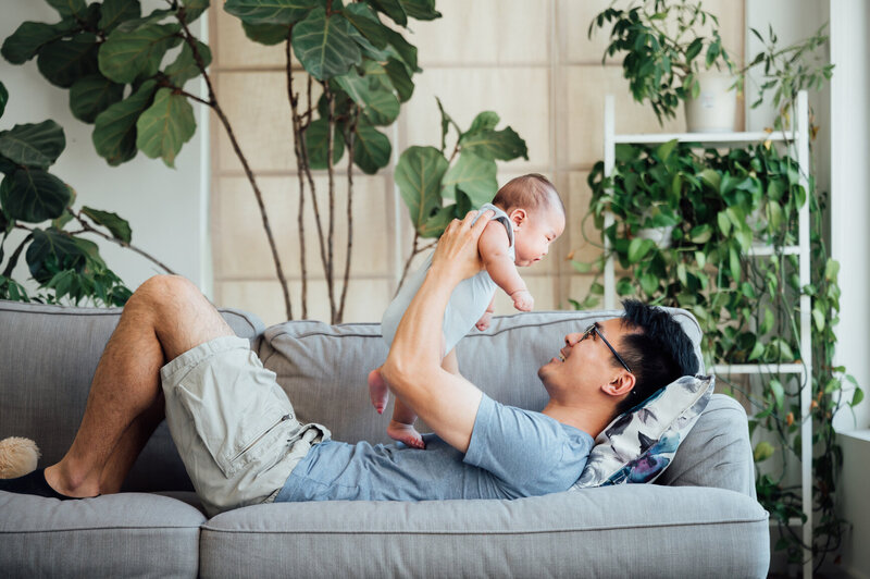 father laying on couch holding and smiling at baby