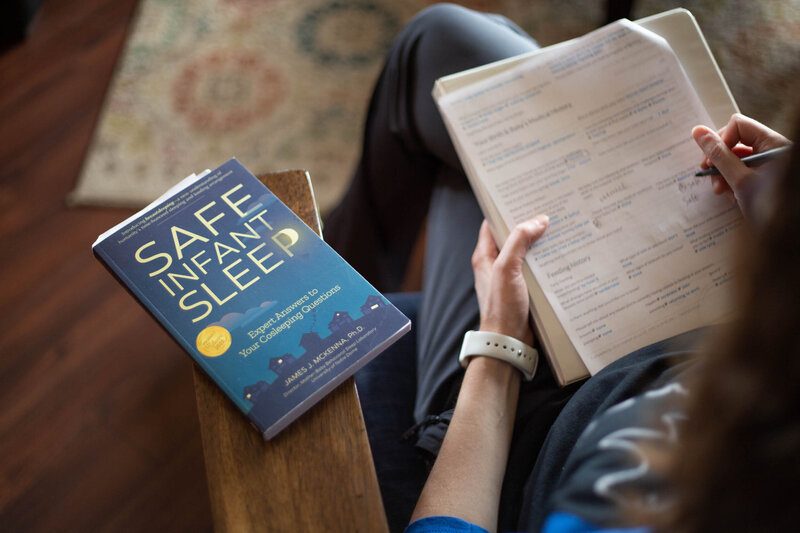 Woman holding a book with a book next to her titled "Safe Infant Sleep"