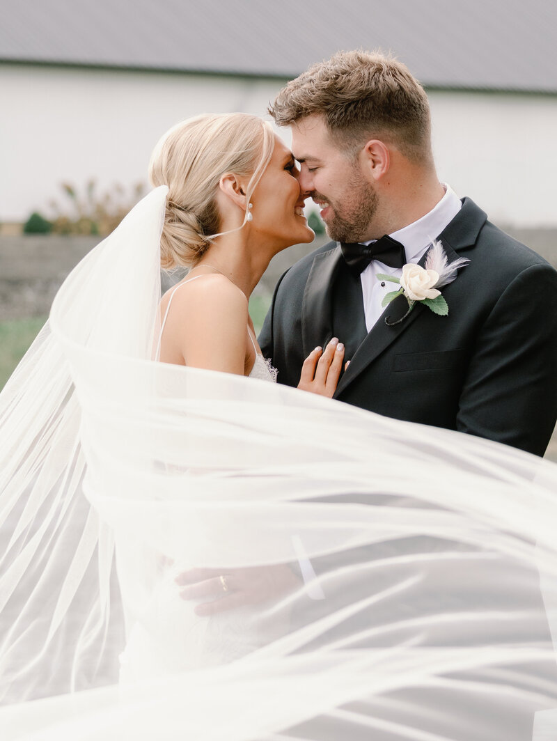 A portrait of a bride and groom with a long veil wrapped around them on their wedding day
