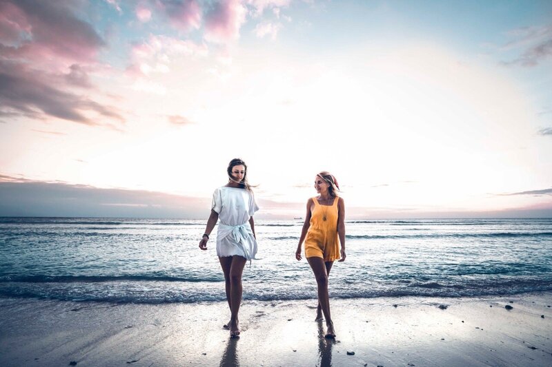 two blonde girls wearing a white dress and an orange jumpsuit in a green field of tall palm trees on Gili trawangan Indonesian Island