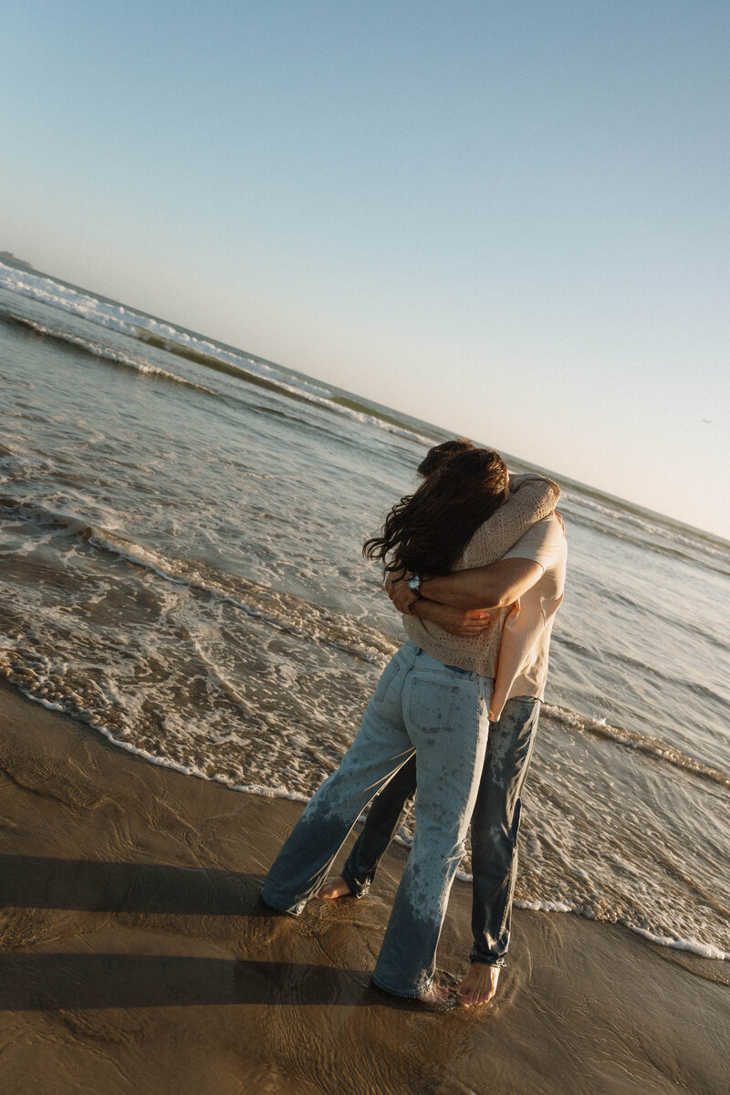 a man and woman hugging by the ocean