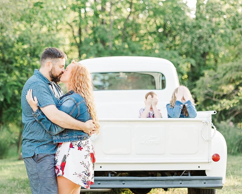 Father and mother kissing with their kids closing their eyes in a white truck for family photos near Erie, PA.