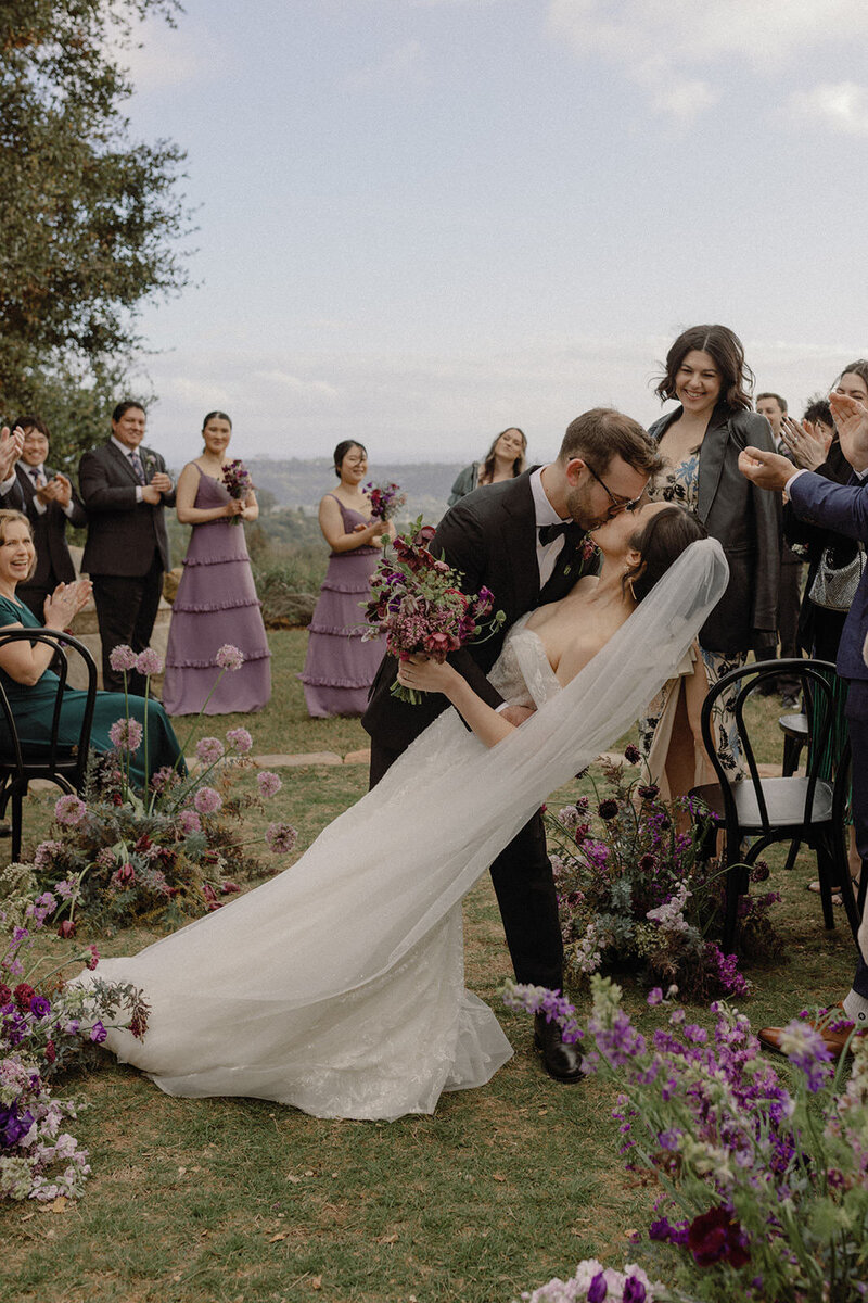 Groom dips his bride for a kiss as they walk back down the aisle after taking vows