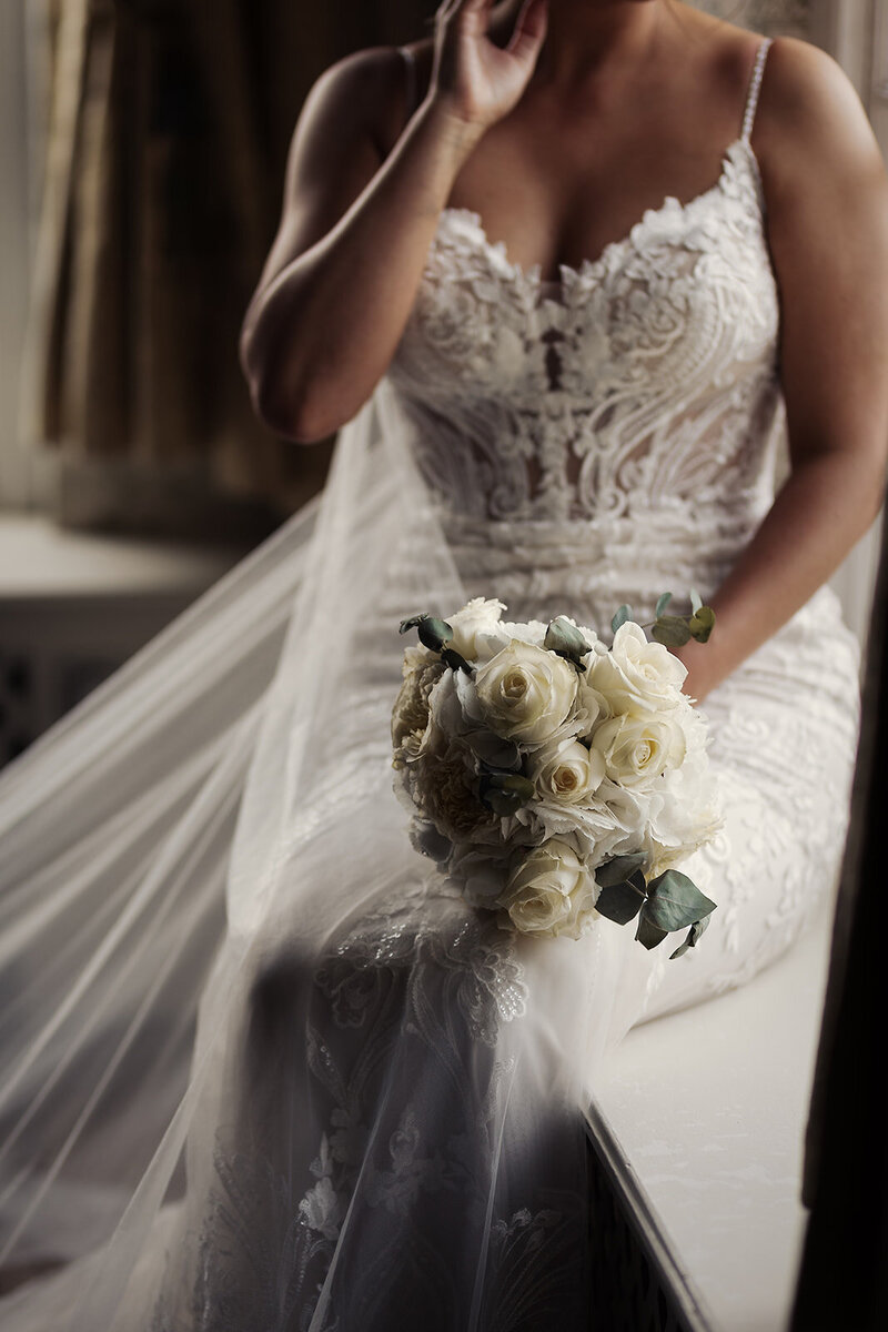A bride sits with her cream rose wedding bouquet.