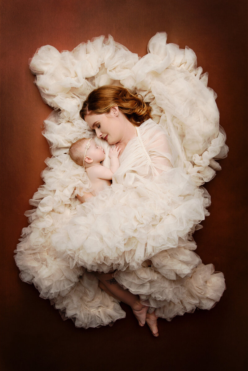 Mom wrapped in luxurious gown holder her baby close to her with eyes closed