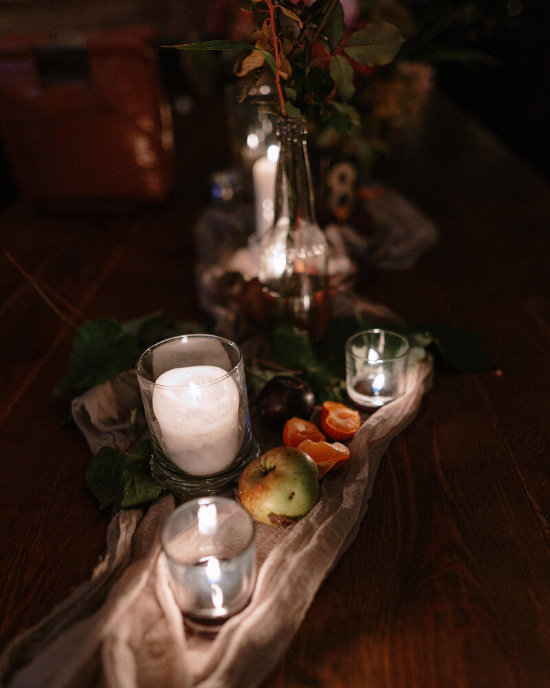 A cozy table setting with candles, fresh fruits, and greenery, creating an inviting and warm ambiance.